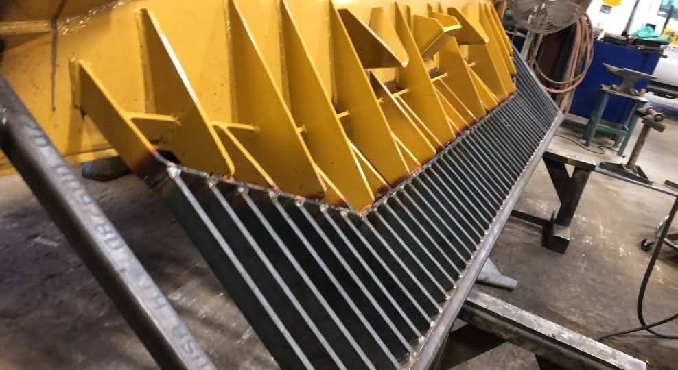 Steel rake tines welded onto a yellow dozer blade