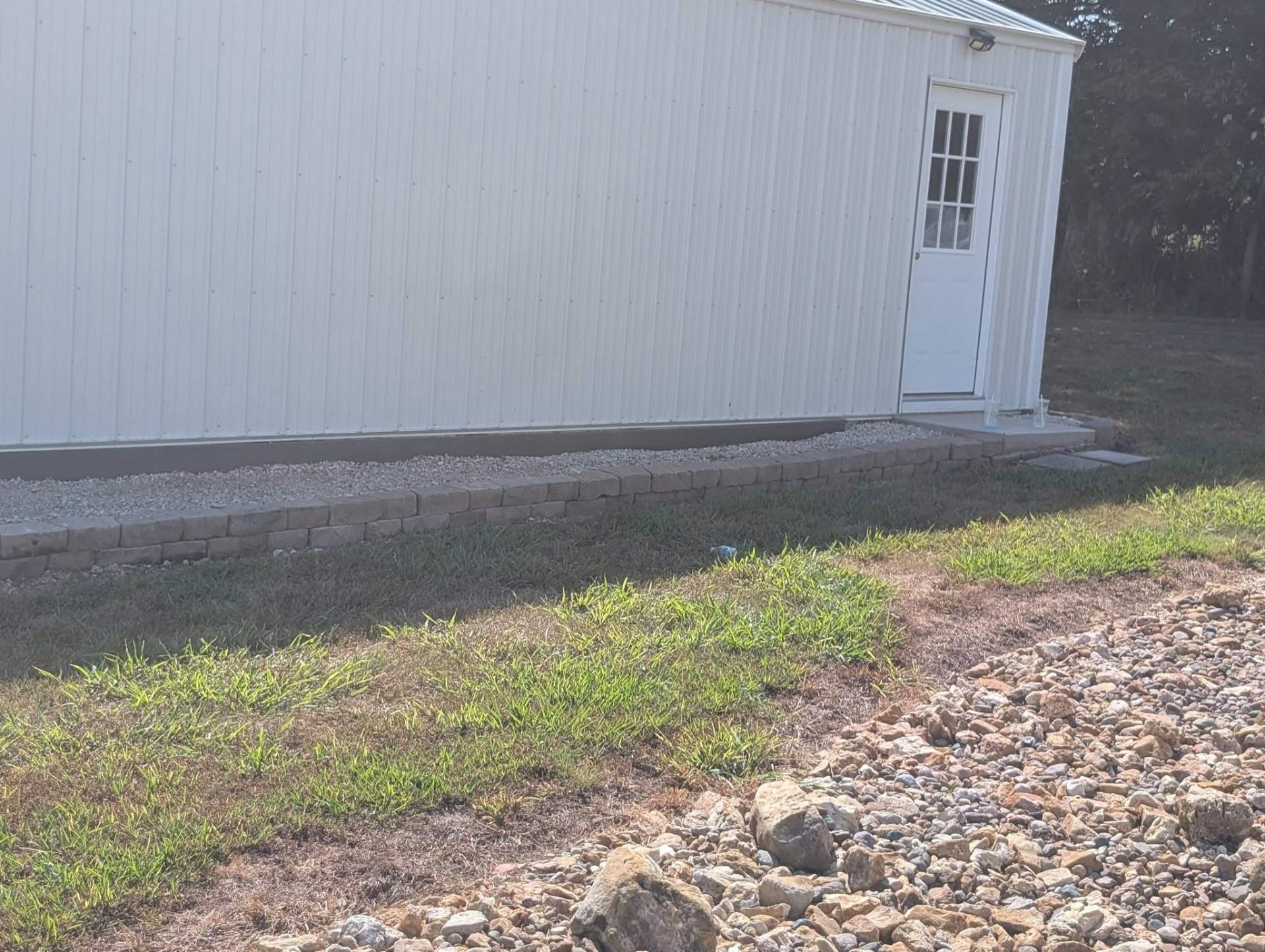 Gravel border with curved block edging running along the base of a white metal shed