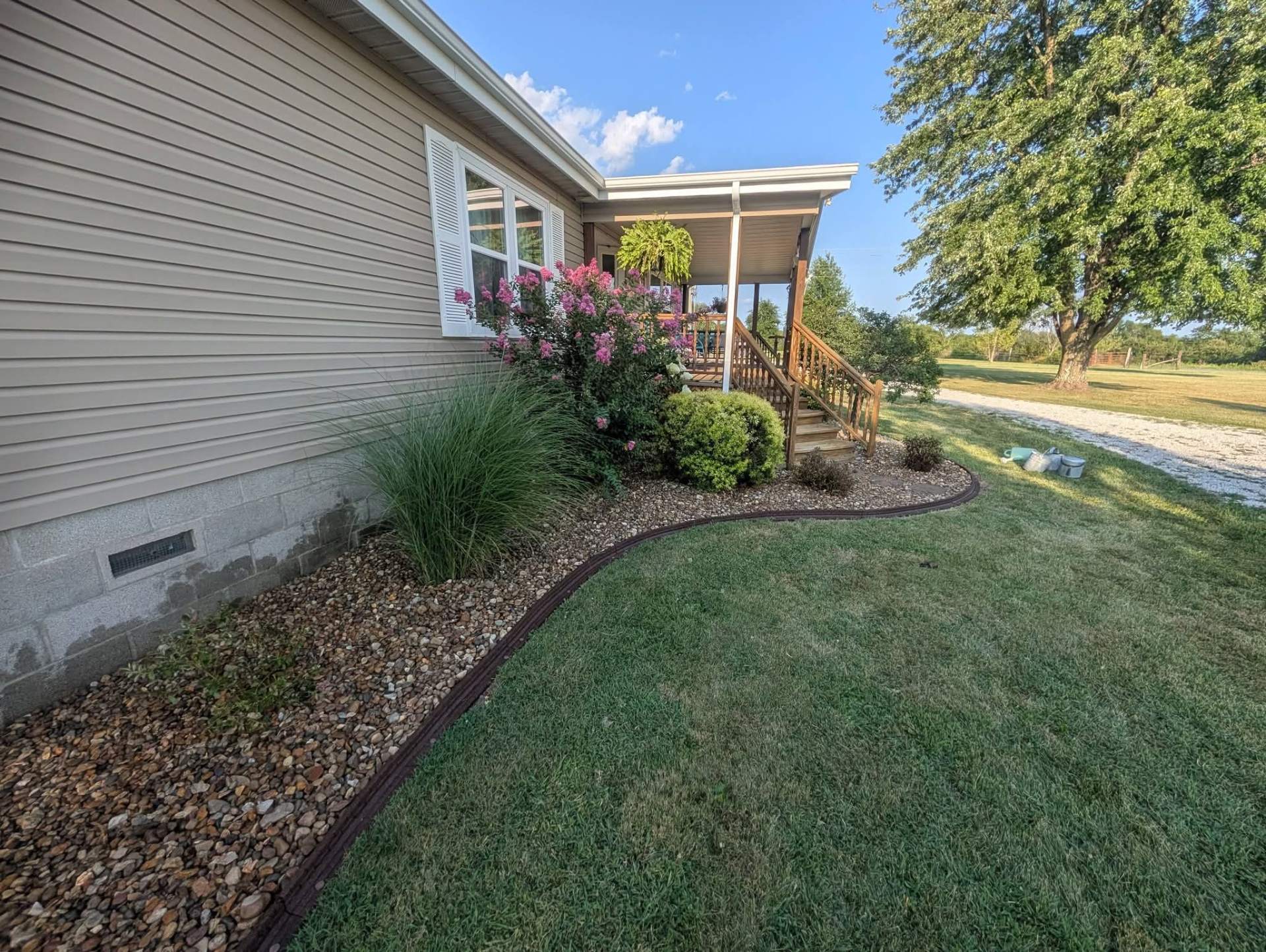 Finished foundation bed with river rock, ornamental grasses, and pink flowering shrubs along a home