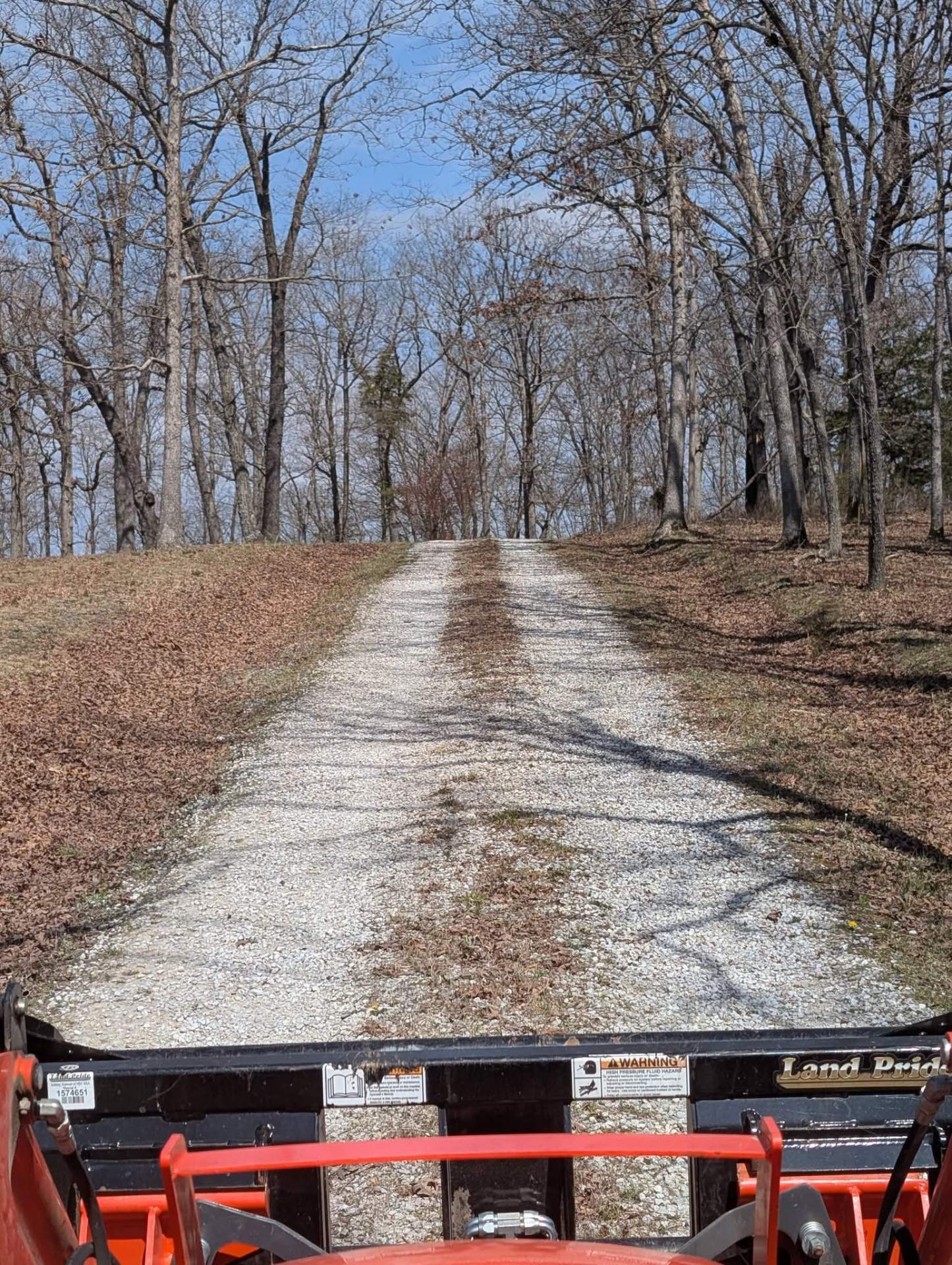 Regraded gravel driveway stretching uphill through bare trees, seen from the tractor