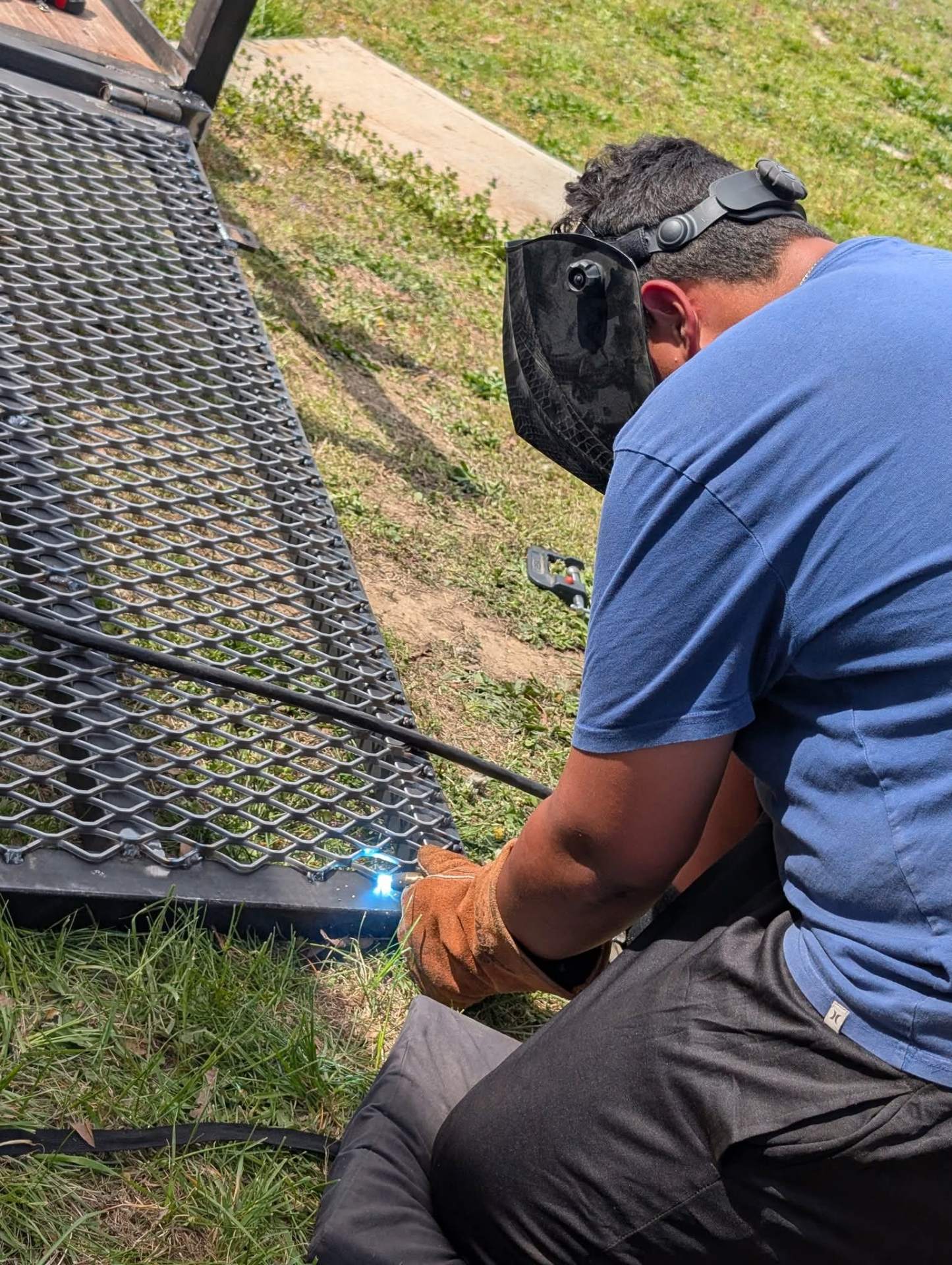 Welder repairing an expanded metal trailer gate on site