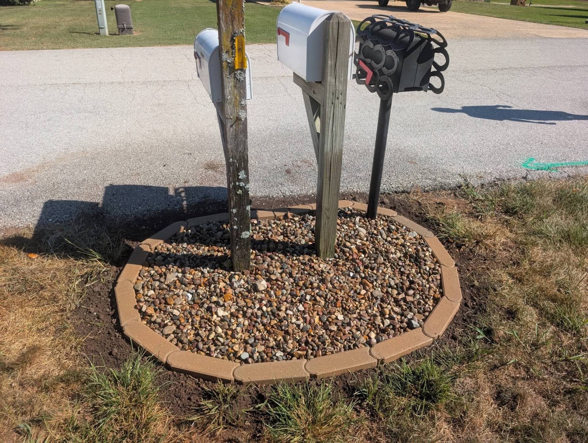 Mailbox island bed edged with scalloped pavers and filled with multicolored river rock