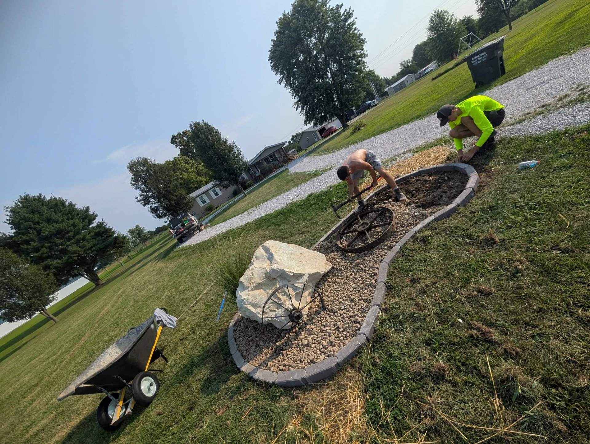 Irizarry crew installing a curved stone bed with a large boulder and decorative wheels
